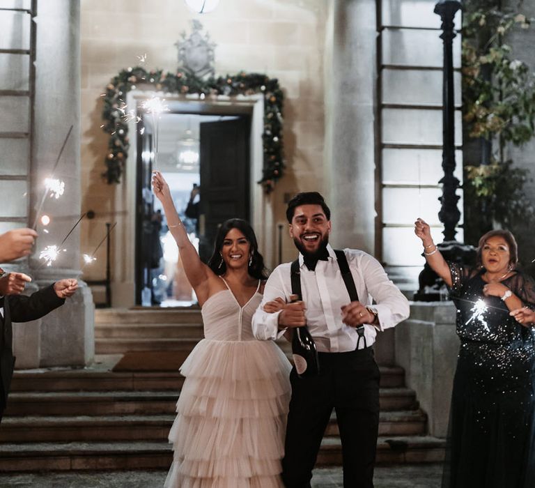 Sparkler send off for bride in ruffle wedding reception dress walking with the groom in white tuxedo 