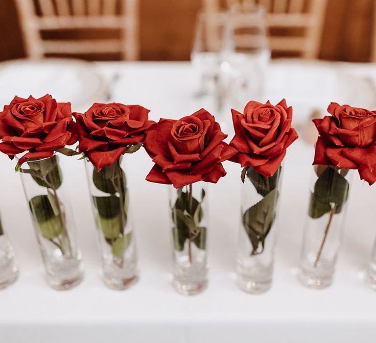 Single stem red roses in vases decorating the wedding top table 