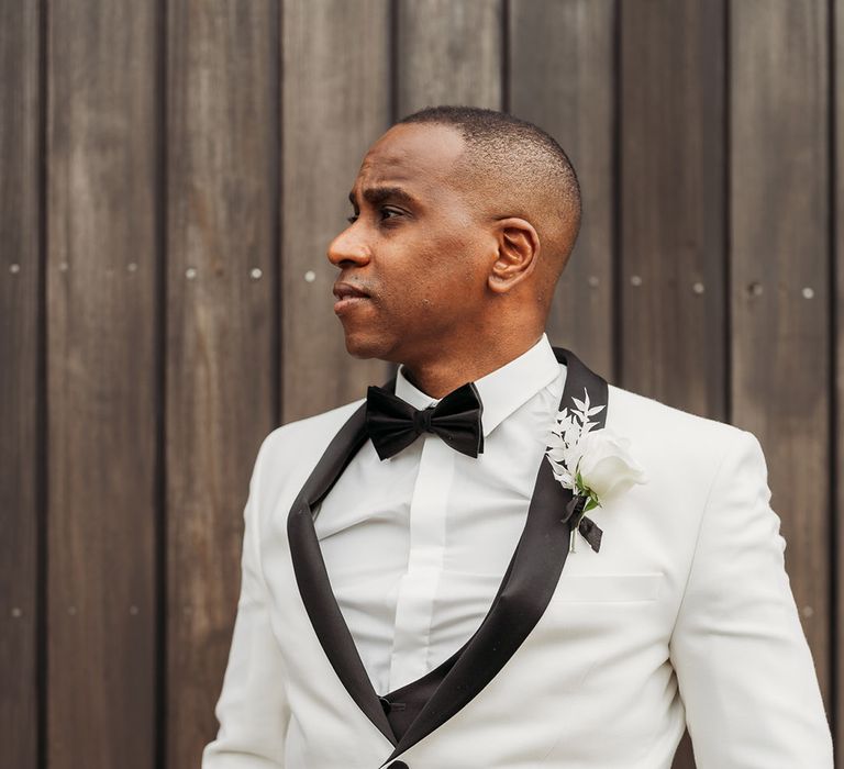 Groom in a white tuxedo jacket, black bow tie, and white rose button hole accessory