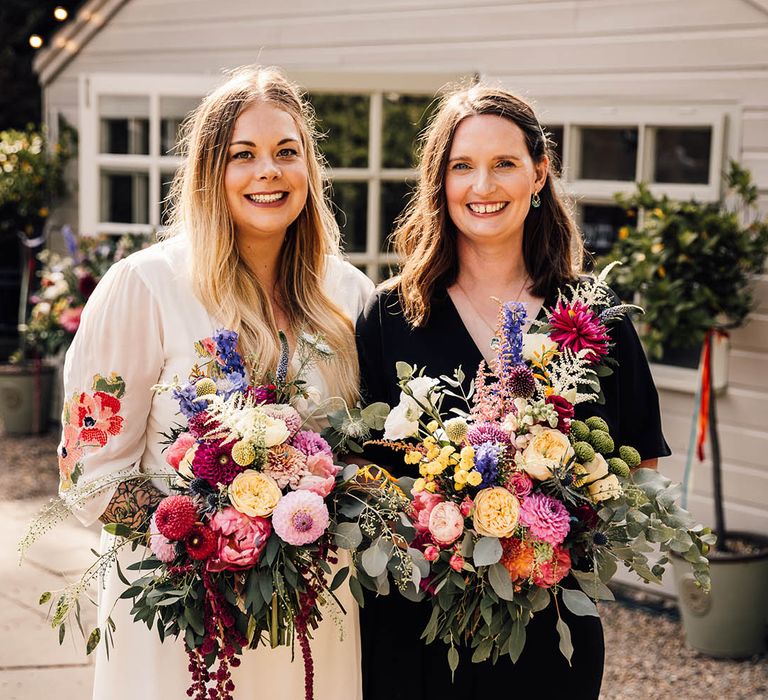 Bride in colourful embroidered wedding dress with bride in black wedding jumpsuit for same sex wedding day 