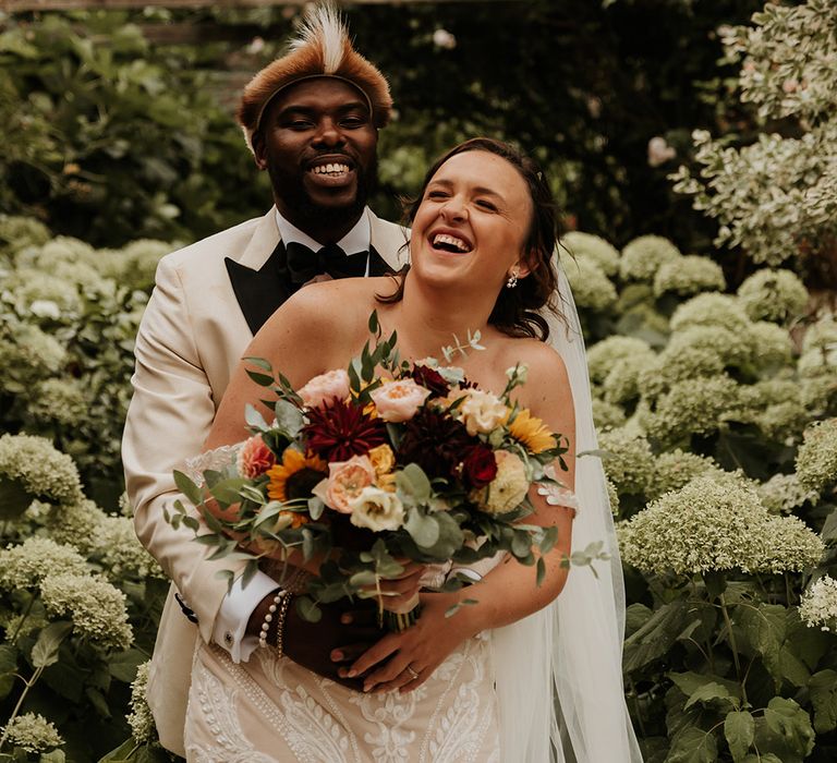 Groom in white tuxedo embracing bride from behind for romantic couple portrait 