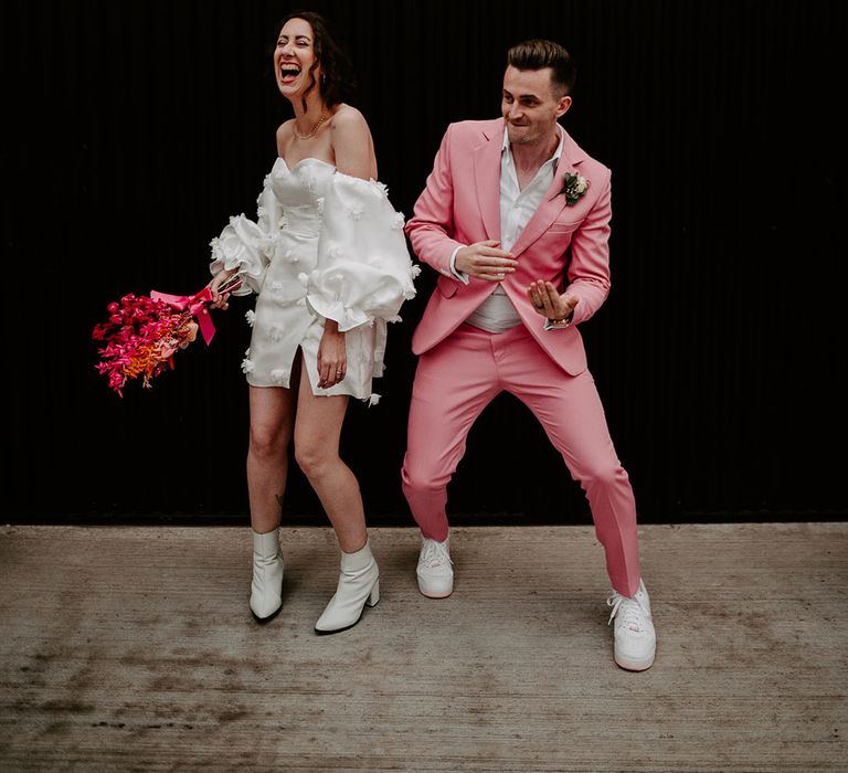 Bride in short wedding dress with bow and white pointed boots with the groom in a pink suit at retro theme wedding 