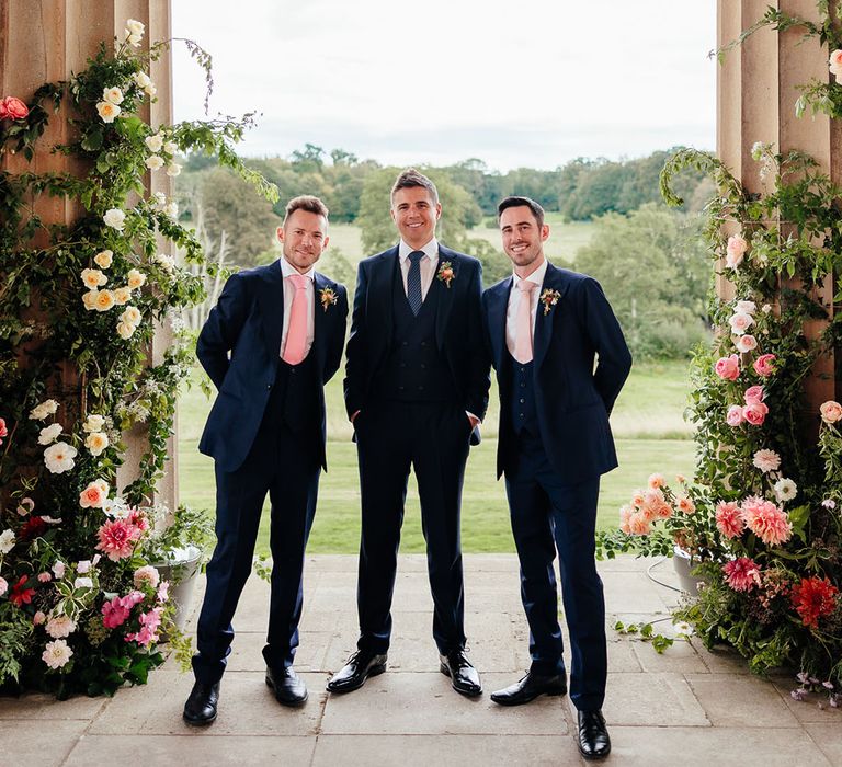 The groom and groomsmen in blue suits stand together waiting for the outdoor ceremony start