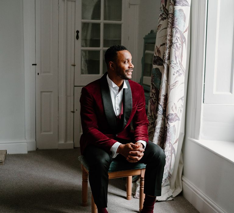 The groom wears a red velvet suit jacket tuxedo for the black tie winter wedding at Berkeley Castle 