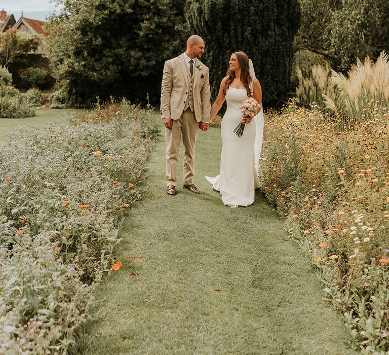 Groom in beige wedding suit with bride in satin slip wedding dress holding pink rose bouquet at home wedding 