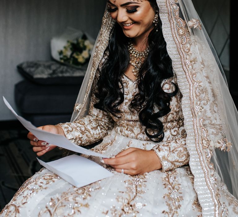 Bride on wedding morning reading a note from her groom in an Ivory gown and veil embellished with traditional Indian embroidery and gold work