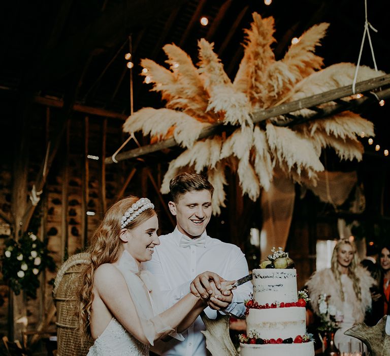 Bride and groom cutting the wedding cake at barn reception 