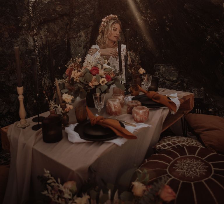 Bride in flower crown and bohemian wedding dress sits at intimate table setting