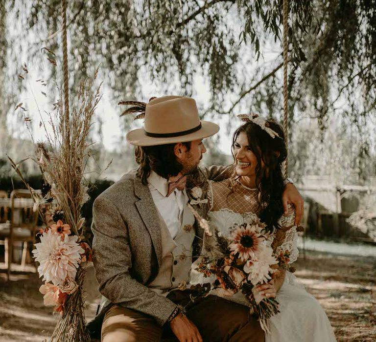 Bride and groom sitting on a wooden tree swing decorated with dried flowers