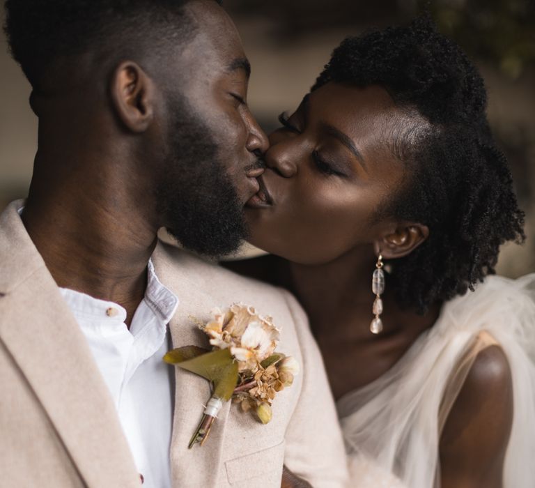 Bride and groom portrait kissing showing off the grooms buttonhole and brides earrings 