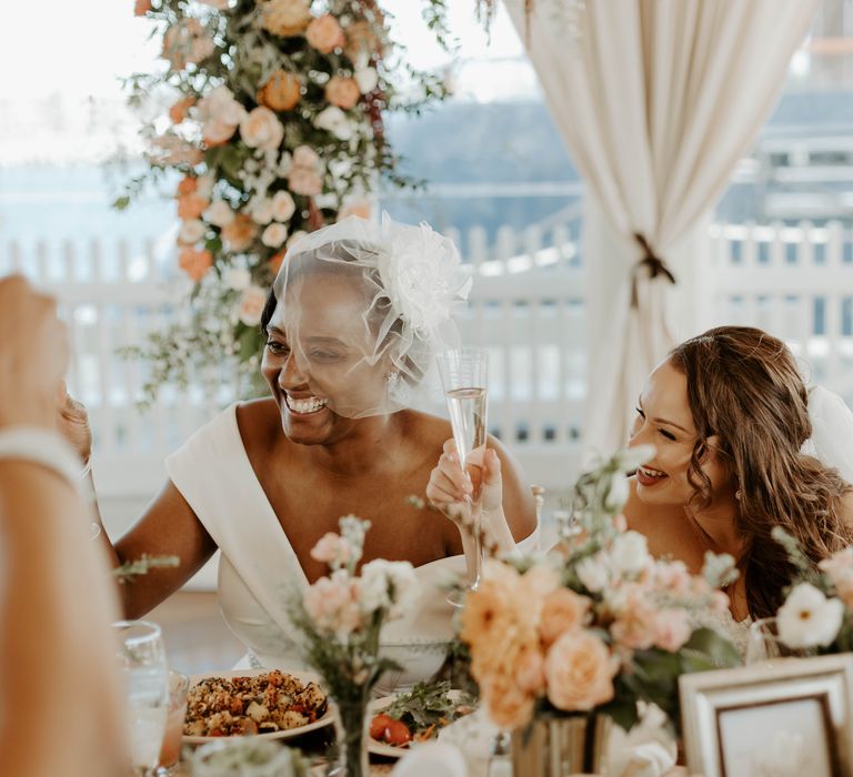 Two brides raising their glass of champagne at their intimate wedding reception with blush pink and peach flowers 