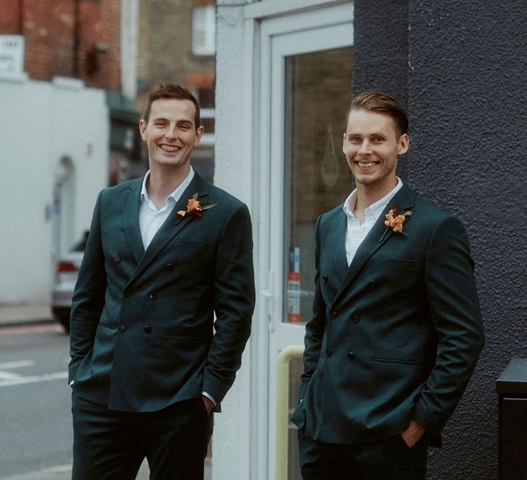 Groomsmen in dark teal suits with orange buttonhole flowers 