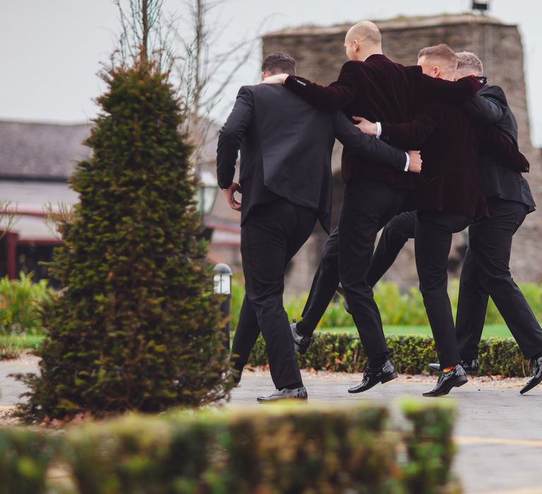 Groomsmen in tuxedos skipping around the gardens at Darver Castle