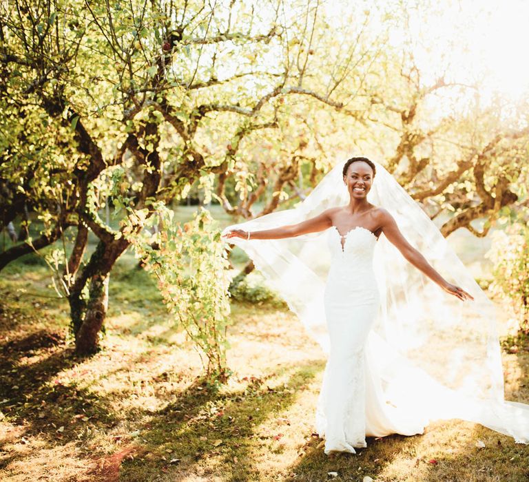 Black bride in sweetheart neckline lace gown spins in the countryside with veil blowing in the wind