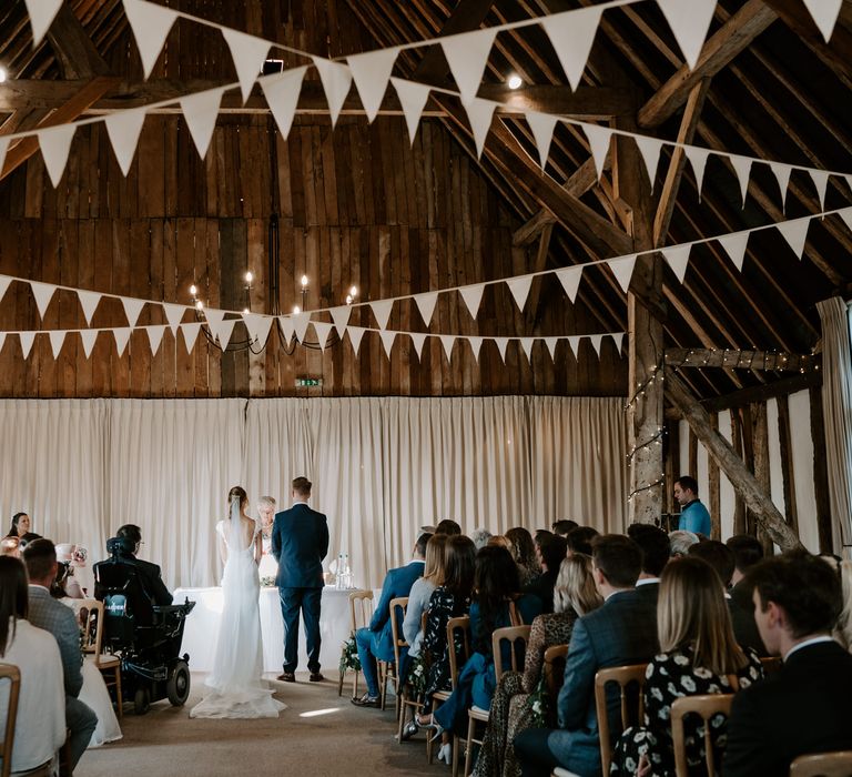 Bride in a fitted wedding dress with low back design and groom in a navy suit standing at the altar 