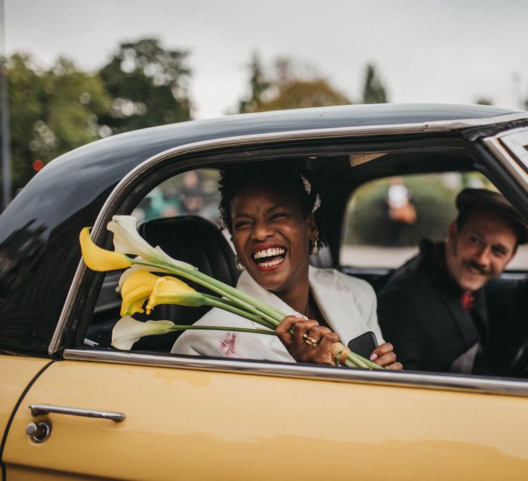 Smiley bride in a yellow wedding car holding yellow and white calla lilies 