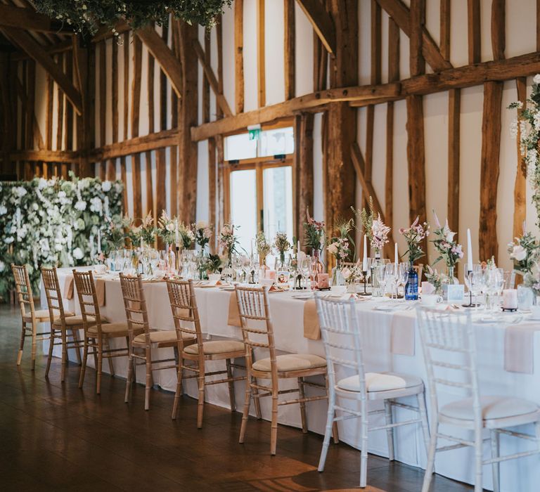 Wedding table featuring white tablecloth surrounded by white floral bouquets 