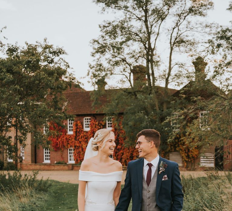 Bride & groom laugh together as they walk through the grounds of the venue