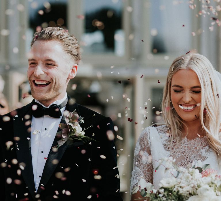 Bride in white Charlie Brear wedding dress and white Augusta Jones lace top and groom in black velvet Hugo Boss suit walk through confetti at Caswell House wedding