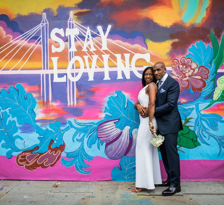 Groom in a navy Tom Ford Suit embracing his bride in a fitted Roland Mouret dress in front of some graffiti art