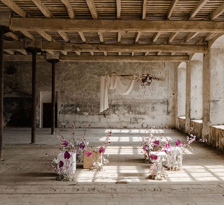 Industrial warehouse wedding ceremony with purple floral arrangements and hanging drift wood altar 