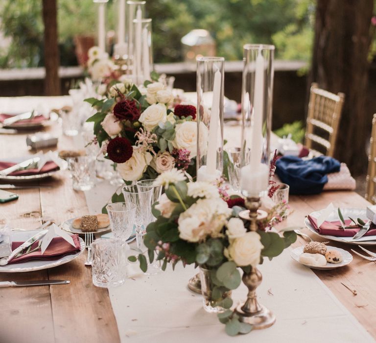 Rustic table setting on wooden table with accent deep red colour and large white candles