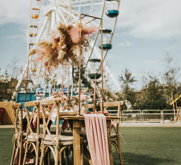 Outdoor tablescape at Dreamland Margate with pink linen table runner, taper candles and pampas grass installation 