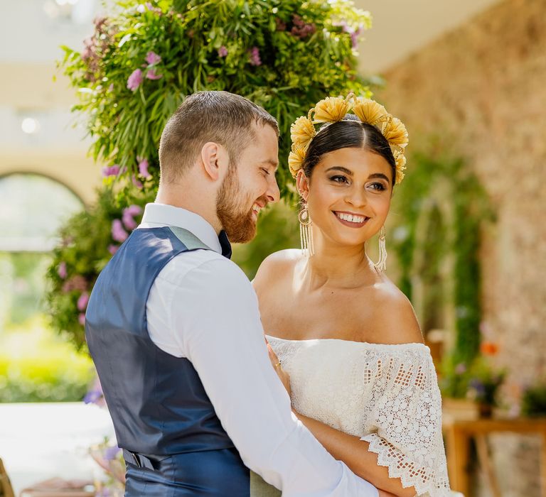 Bride in an off the shoulder layered wedding dress with middle parted bridal updo and yellow headdress 