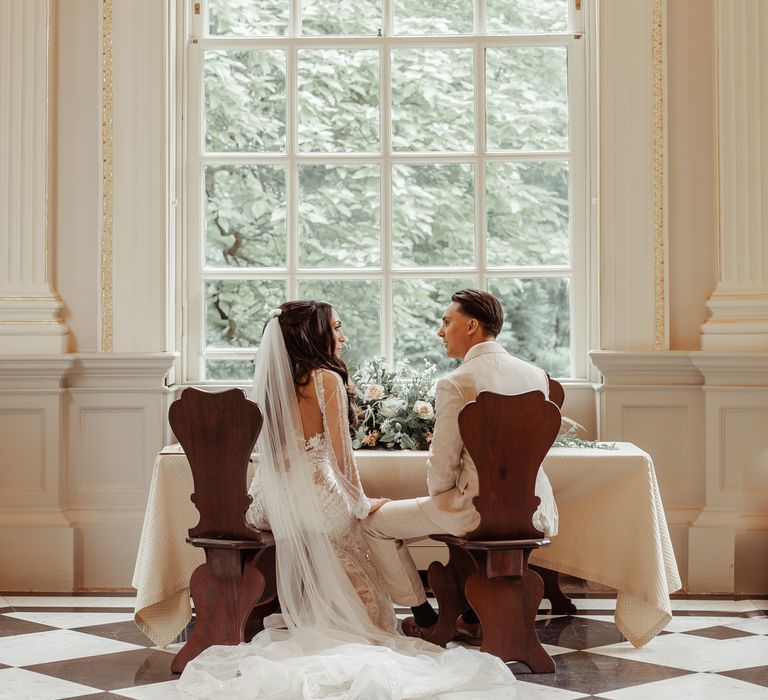 Bride & groom sit in front of large window after wedding ceremony