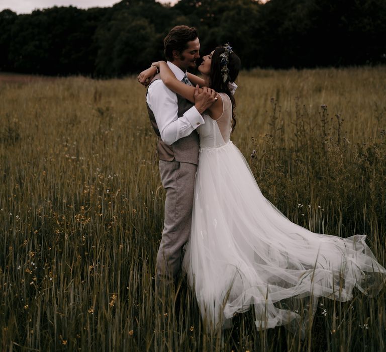 Bride & groom embrace in green fields for post-wedding portraits together