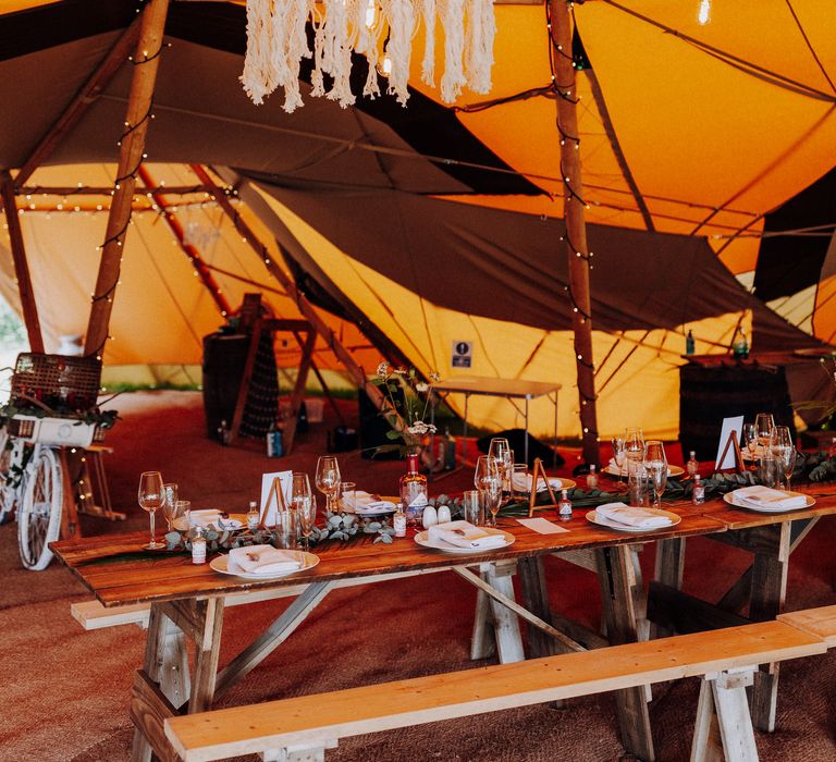 Macrame shade hangs from tipi with lights above wooden tables 