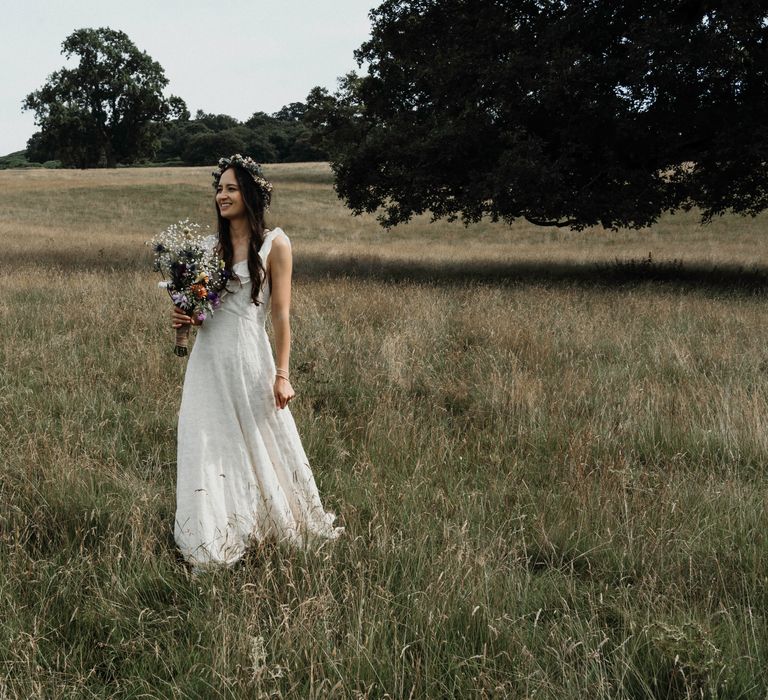 Bride walks through fields on her wedding day whilst wearing Sézane wedding gown complete with floral crown