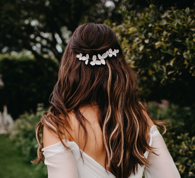 Bride with long wavy hair wearing a delicate flower headdress showing on the gathered detail on the Suzanne Neville Molly wedding dress 