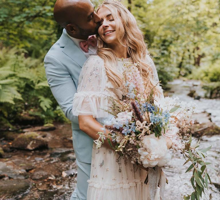 Groom wraps his arms around bride as she holds pastel floral bouquet