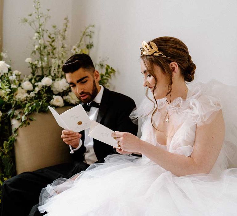 Bride in a fluffy tulle wedding dress with gold laurel crown sitting on a chaise lounge with her groom in a tuxedo 