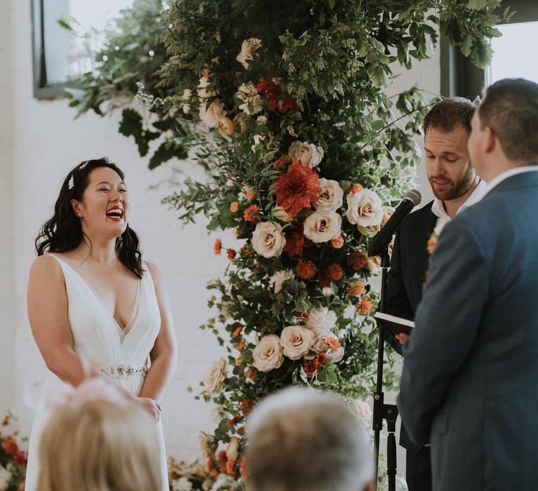 East Asian bride in an A line wedding dress with a plunging neckline smiling during the wedding ceremony 