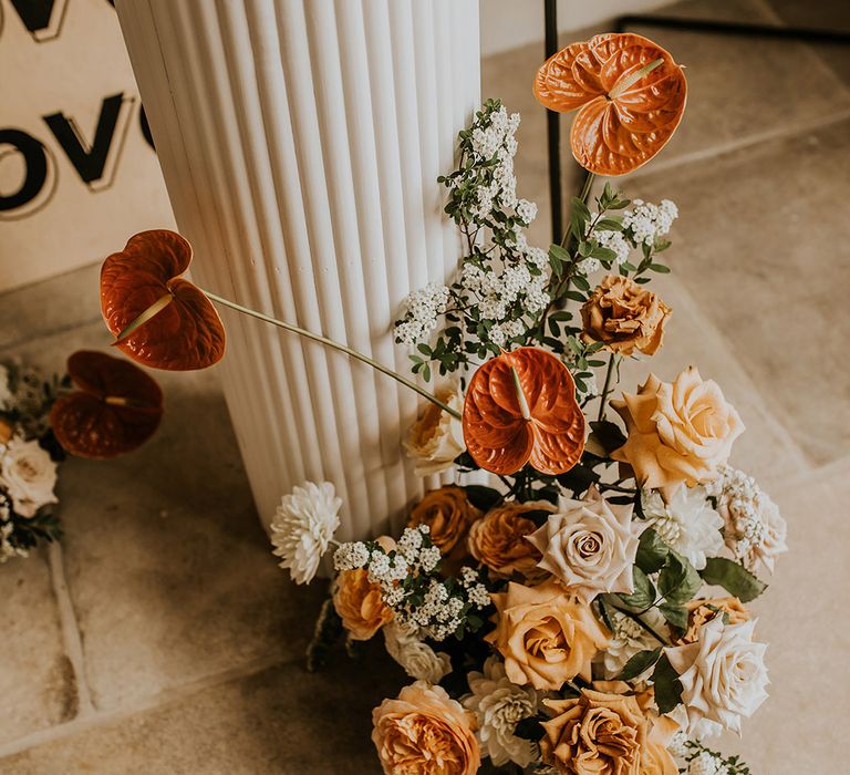 Orange, peach and cream wedding flower arrangement at the foot of the cake stand 