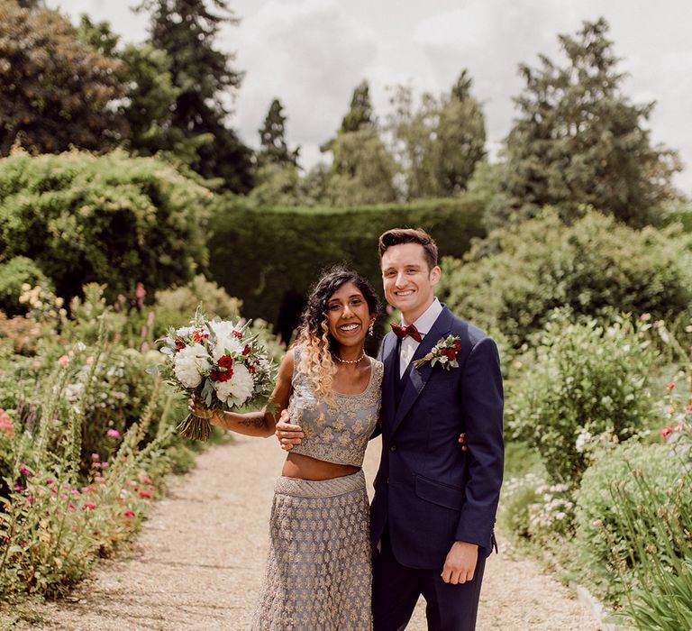 Bride leans into her groom on their wedding day on pathway lined with greenery | Joshua Gooding Photography