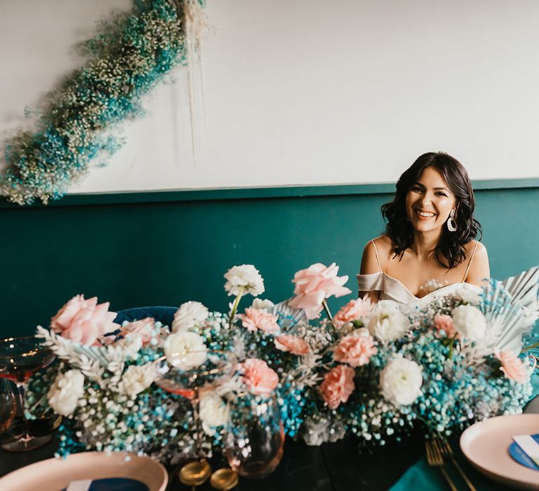 Bride sitting at the reception table with a teal blue gypsophila flower cloud with pink roses and dried palm leaves centrepiece 