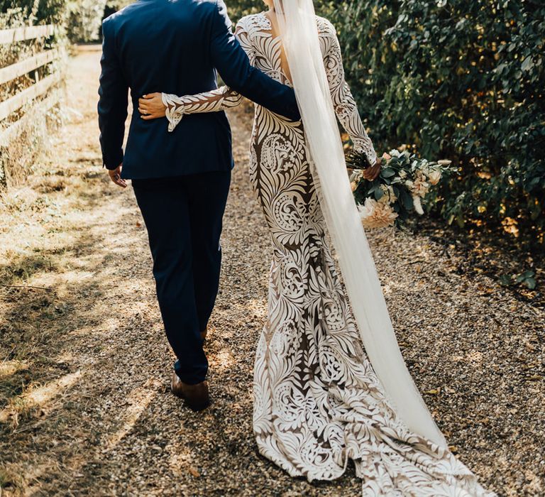 Bride in long Boho wedding dress with veil walking in forest setting with Groom in Navy suit 