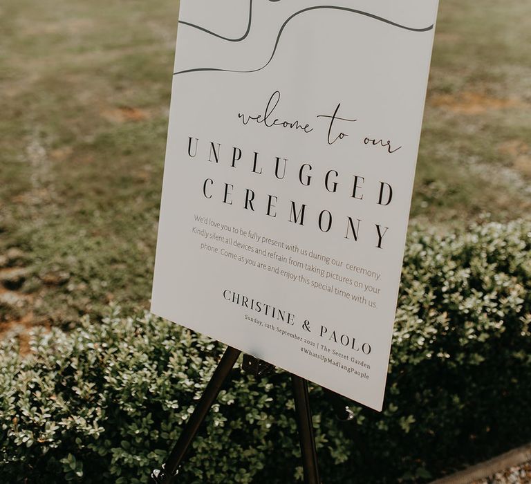 Unplugged Ceremony signage with modern feel and white background sat on lawn outdoors