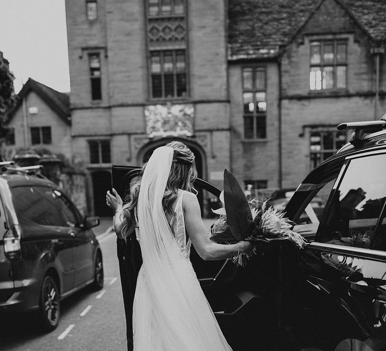 Black & white image of bride getting into car on her wedding day 