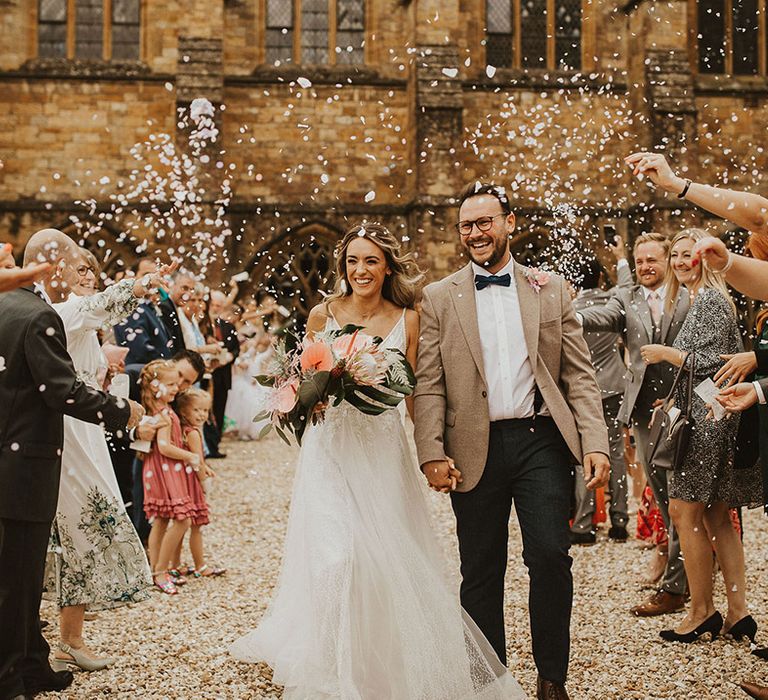 Bride & groom walk together on their wedding day as wedding guests throw confetti around them