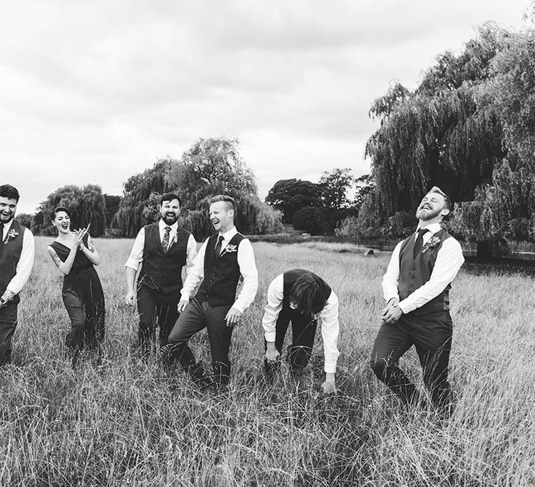 Black & white image of groomsmen in field laughing with one another