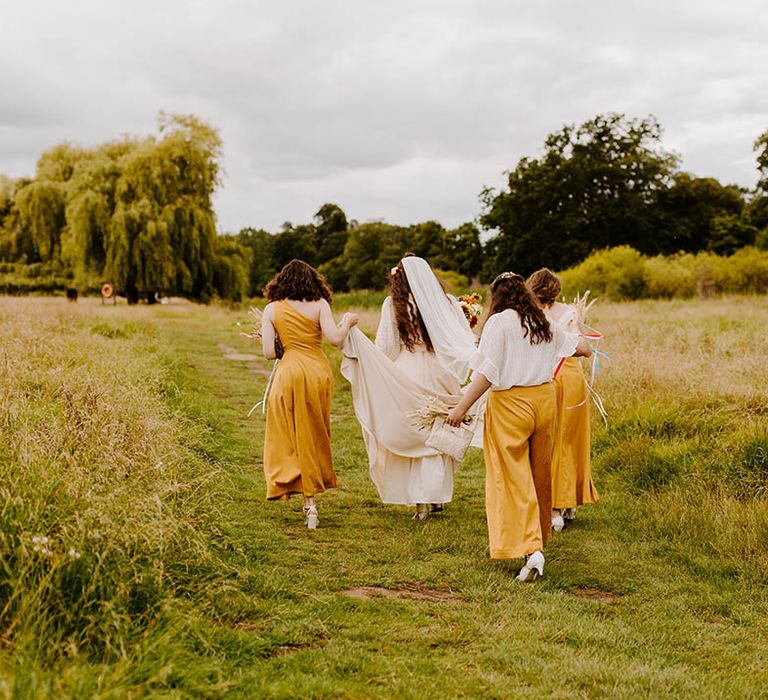 Bride walks with her bridesmaids who wear custom dresses on her wedding day through field