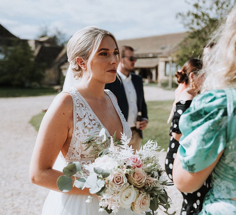 Bride in lace dress clutches blush rose bouquet