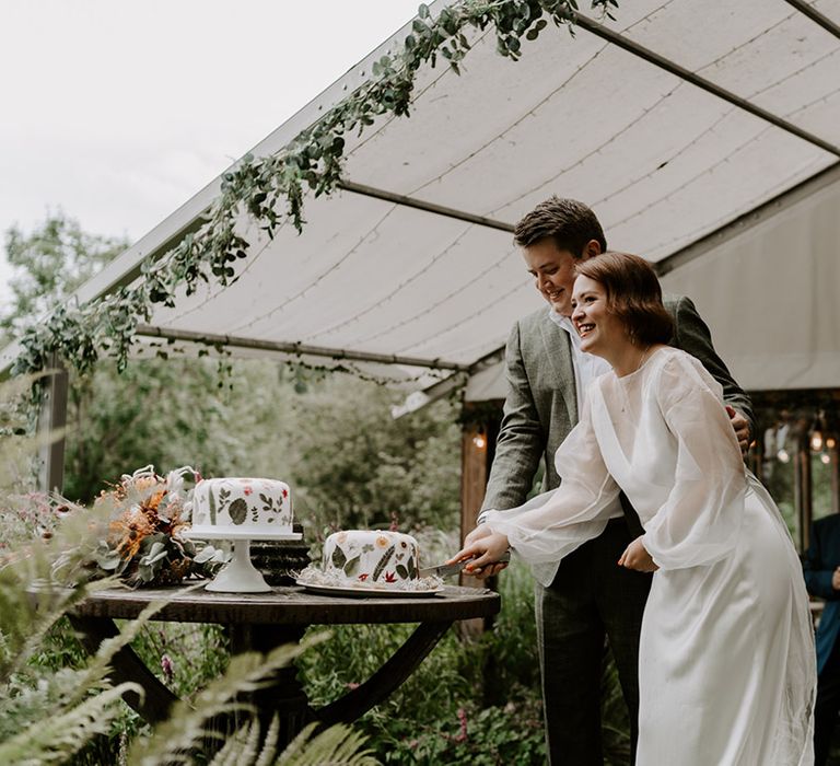 Bride in a sheer long sleeve wedding dress cutting the flower pressed wedding cake at The Copse Country House wedding 