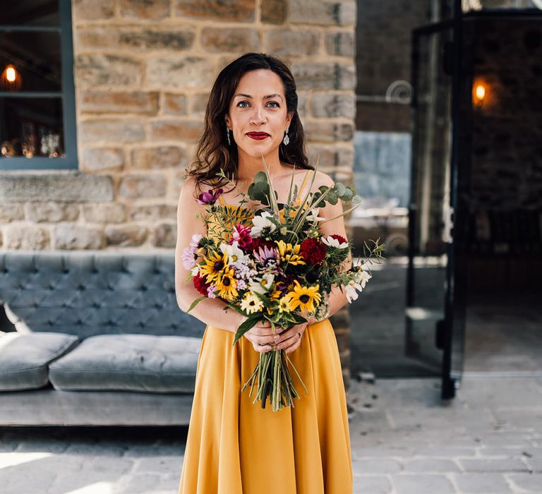 Bride wears yellow wedding dress and holds colourful bouquet