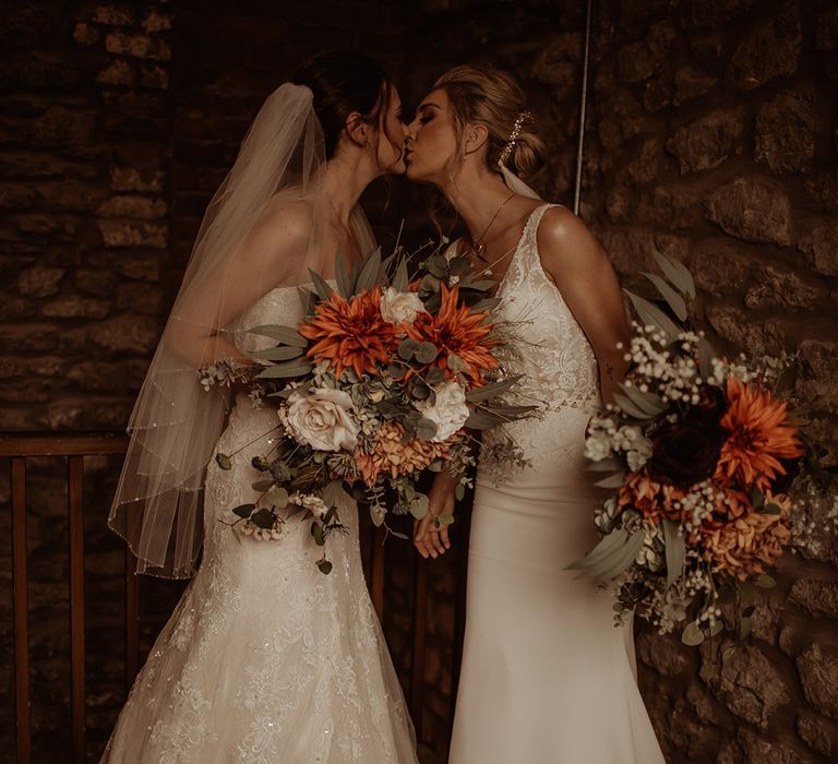 Brides kiss on the day of their wedding as they hold floral bouquets