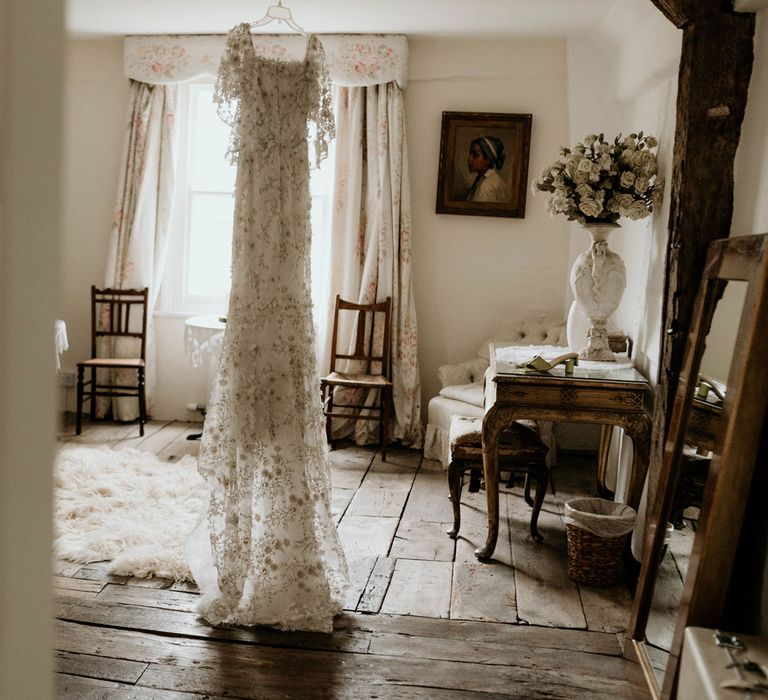 3D flower applique wedding dress hangs in bedroom of old house at Lyde Court in Hereford before wedding